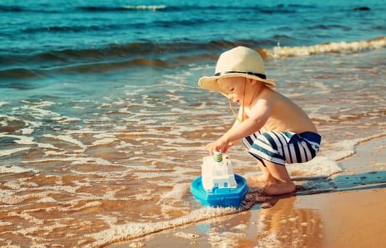 Baby boy playing with ship toy at sea. Child os on vacation in summer at the beach on vacations