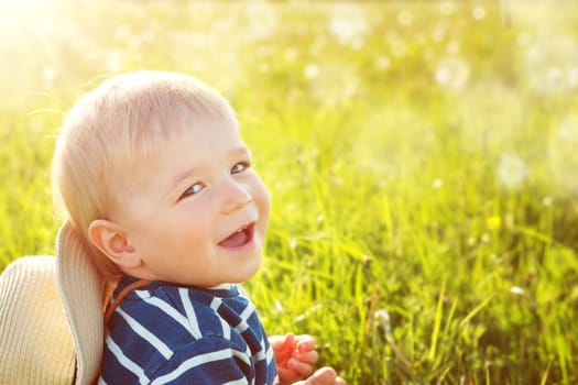 Baby boy sitting in grass on the fieald with dandelions at sunnysummer evening