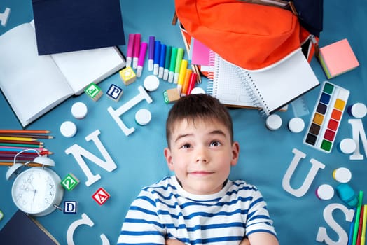 child lying on blue blanket with various school accessories