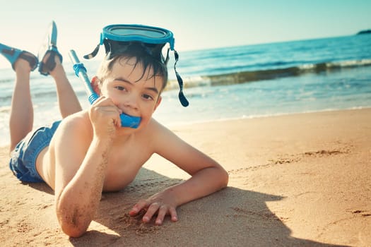 Child lying on the beach with swimming mask and flippers. Boy on vacation at sea