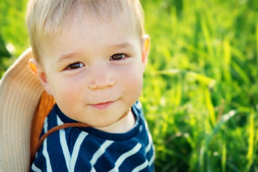 Baby boy sitting in grass on the fieald with dandelions at sunnysummer evening