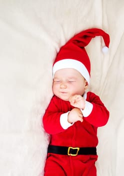 little baby sleeping in red hat on white blanket. Eight month old child in santa costume