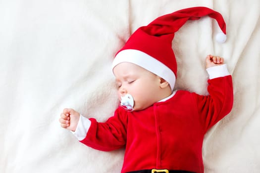 little baby sleeping in red hat on white blanket. Eight month old child in santa costume