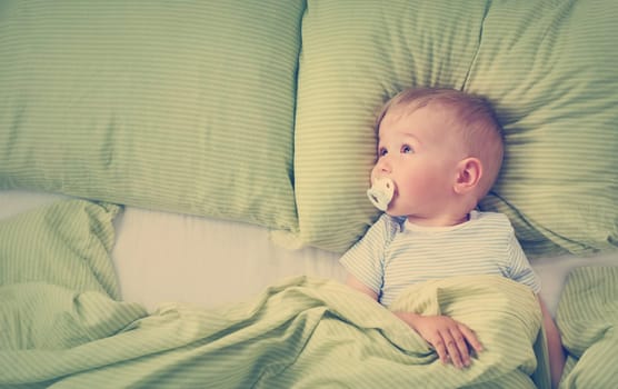 One year old baby lying in the bed with green bedding