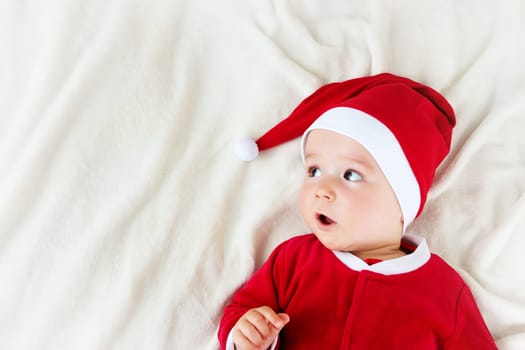 little baby lying in red hat on white blanket. Eight month old child in santa costume