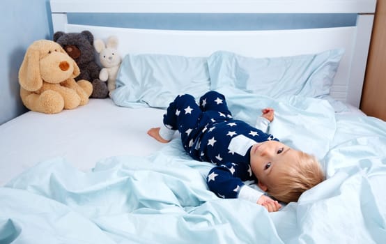 One year old baby in pyjamas lying in the bed with blue bedding