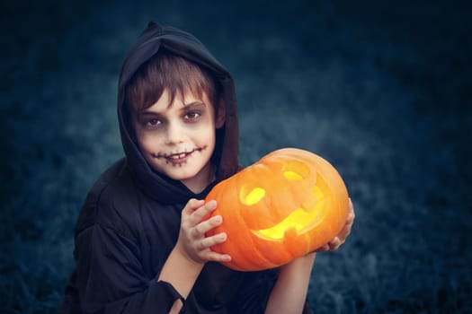 Child in scary costume holding pumpkin ln. Child in halloween outfit at night