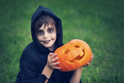 Child in scary costume with pumpkin. Child in halloween outfit playing in the garden