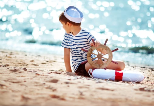 seven years old boy playing at the beach in sailor hat. Child with a steering wheel at sea