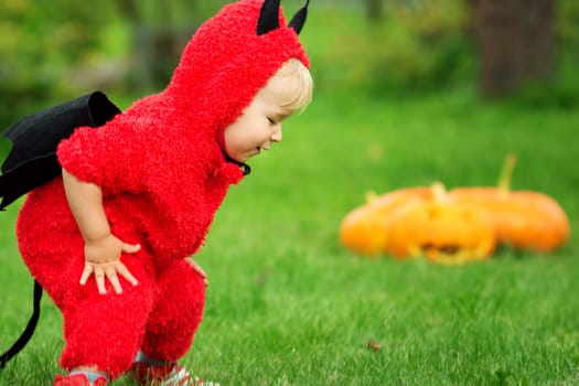 Baby in devil costume with pumpkins. Child in halloween outfit playing in the garden