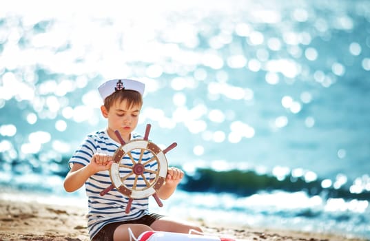 seven years old boy playing at the beach in sailor hat. Child with a steering wheel at sea