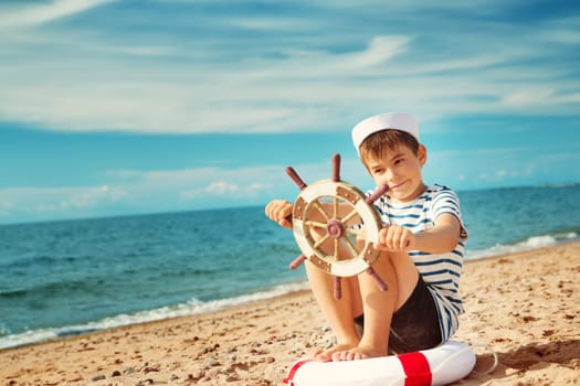seven years old boy playing at the beach in sailor hat. Child with a steering wheel at sea