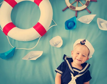 two years old boy playing in sailor hat. Child with paper ships on blue background