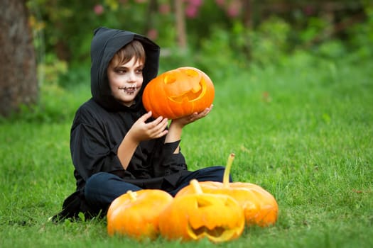 Child in scary costume with pumpkin. Child in halloween outfit playing in the garden