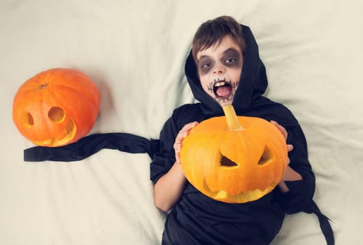 Child in scary costume with pumpkin. Child in halloween outfit on white background