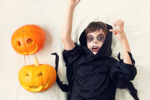 Child in scary costume with pumpkin. Child in halloween outfit on white background