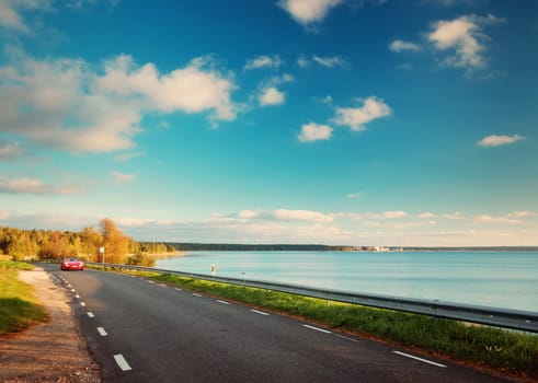 asphalt road with moving car at seaside at sunset