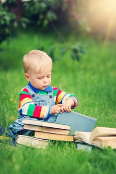 one year old baby reading a book sitting on the grass in garden