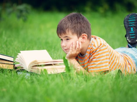 seven years old child reading a book lying on the grass