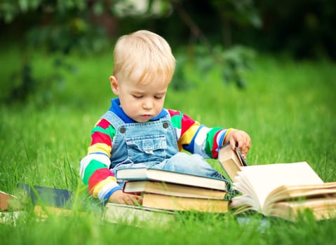 one year old baby reading a book sitting on the grass in garden