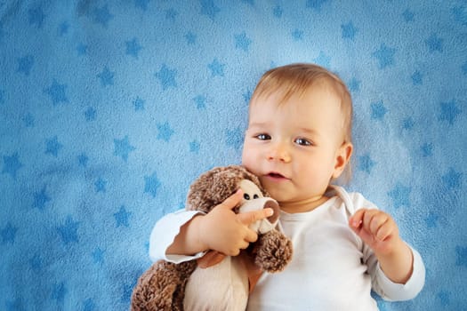 One year old baby lying in bed with a plush teddy bear