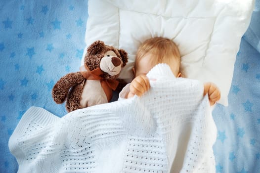 One year old baby lying on blue towel with stars. Child hiding under blanket