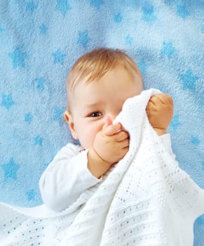 One year old baby lying on blue towel with stars. Child hiding under blanket