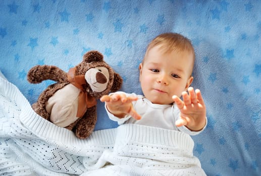 One year old baby lying in bed with a plush teddy bear