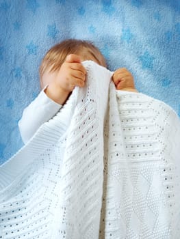 One year old baby lying on blue towel with stars. Child hiding under blanket