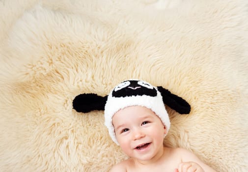 sleepy one year old baby lying in sheep hat on lamb wool background