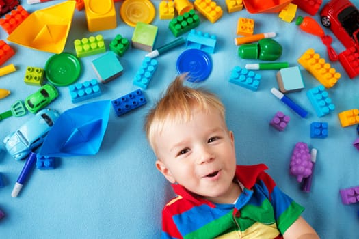 Baby boy lying on blue blanket with many toys around