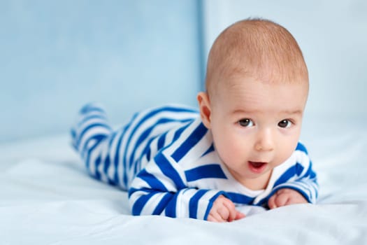 happy little boy lying in the bed. Funny four month old baby in striped sleepsuit at home.