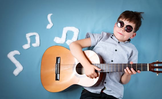 happy seven years old boy on blue blanket background with acoustic guitar and musical notes. Young guitarist singing song