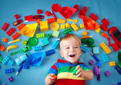 Baby boy lying on blue blanket with many toys around