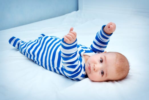 happy little boy lying in the bed. Funny four month old baby in striped sleepsuit at home.
