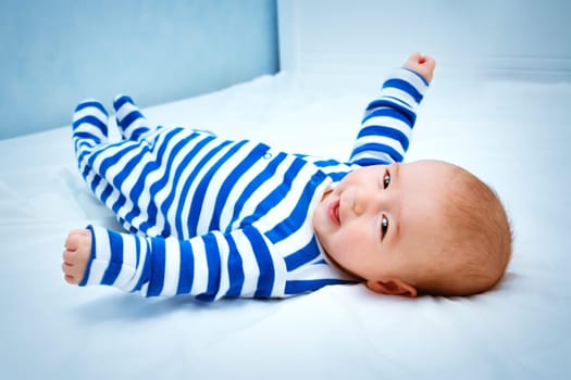 happy little boy lying in the bed. Cute four month old baby in striped sleepsuit at home.