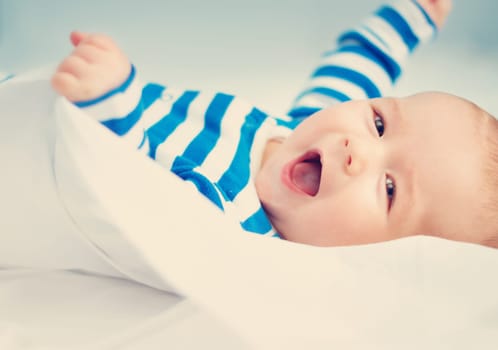 happy little boy lying in the bed. Cute four month old baby in striped sleepsuit at home.
