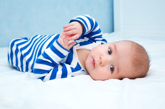 happy little boy lying in the bed. Funny four month old baby in striped sleepsuit at home.