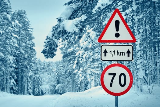 winter view on the road through coniferous forest. Road caution sign in forest landscape