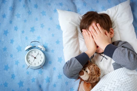 six years old child sleeping in bed on pillow with alarm clock and a teddy bear