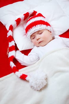 Sleepy baby on red blanket in knitted hat. Cute child sleeping in christmas cap