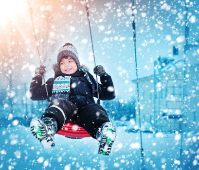 Boy in knitted hat, gloves and scarf outdoors at snowfall. Child in winter clothes