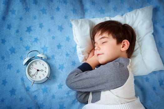 six years old child sleeping in bed on pillow with alarm clock and a teddy bear