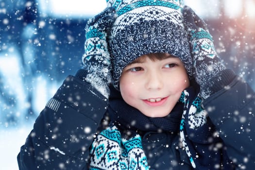 Boy in knitted hat, gloves and scarf outdoors at snowfall. Child in winter clothes