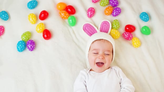 Baby boy in bunny hat lying on green blanket with multicolored easter eggs