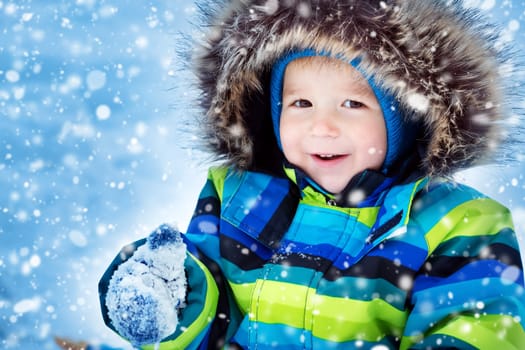 Baby boy smiling at snowfall. Child in winter clothes