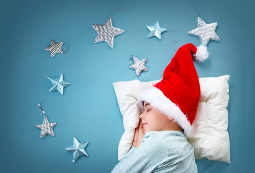 Sleepy child on blue blanket in red hat. Cute boy sleeping in christmas cap