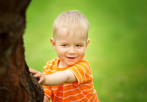 Happy little boy playing in the garden. Child hiding under tree in summer