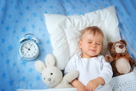 One year old baby lying in bed with alarm clock