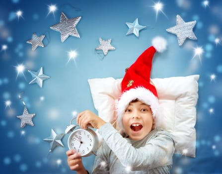 Happy child on blue blanket in red hat. Cute boy in christmas cap with alarm clock